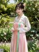 A woman in a pink and green hanbok standing in a garden.