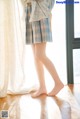 A woman standing in front of a window wearing a plaid skirt.