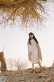 A woman standing in front of a tree wearing a white dress.