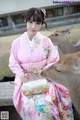 A woman in a pink kimono sitting next to a deer.