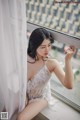 A woman in a white lingerie sitting by a window.