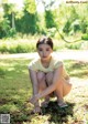 A young woman crouching down on the ground in a park.